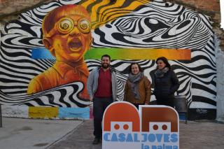 La regidora Montserrat Flores (centre) i dues persones responsables del Casal de Joves davant un mural de 